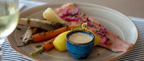 A plate with salmon, vegetables, and a small bowl of sauce on a striped tablecloth.