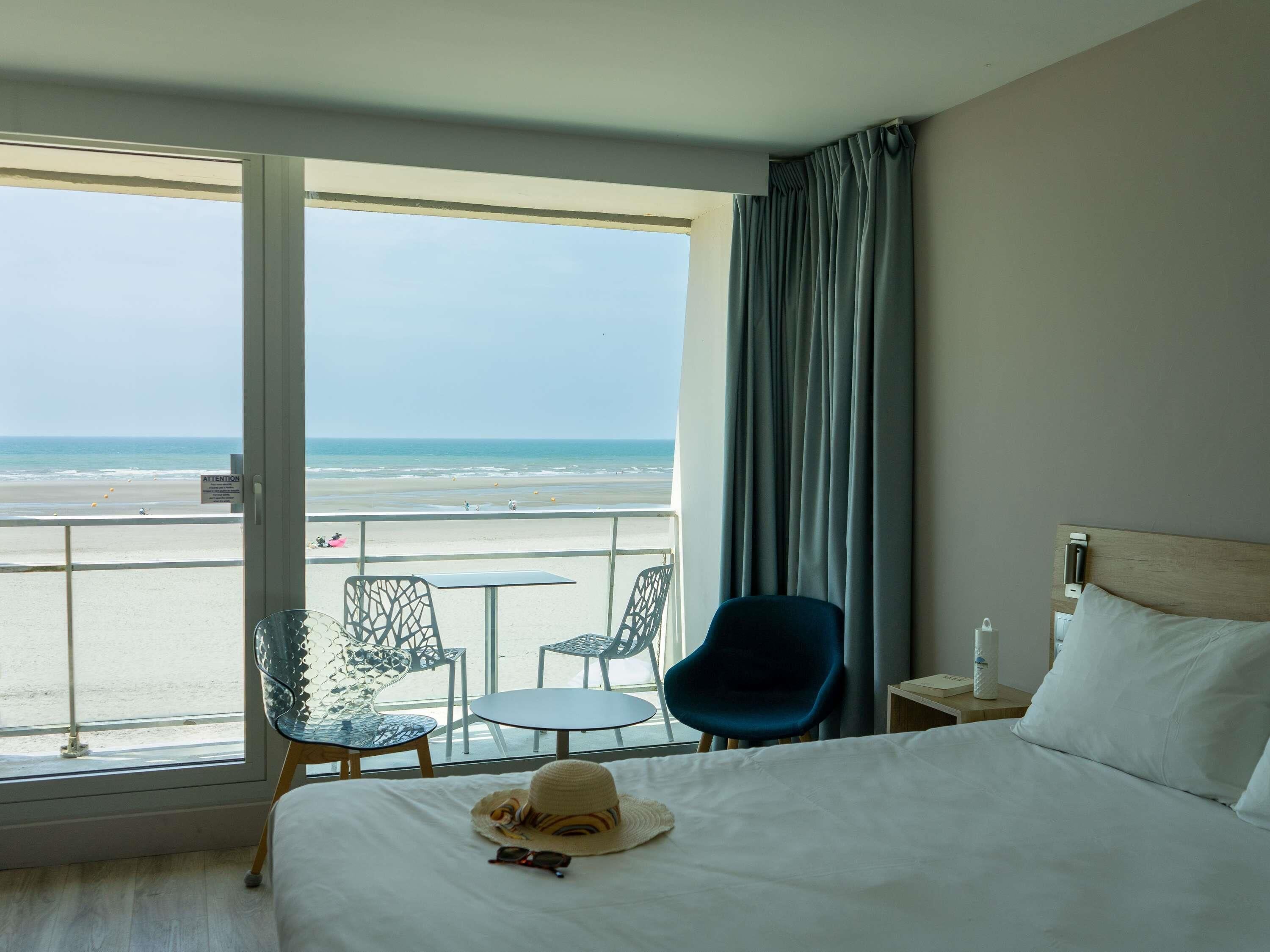 Ein Hotelzimmer mit einem Bett, einem Fenster mit Blick auf den Strand, einem Tisch und zwei Stühlen.