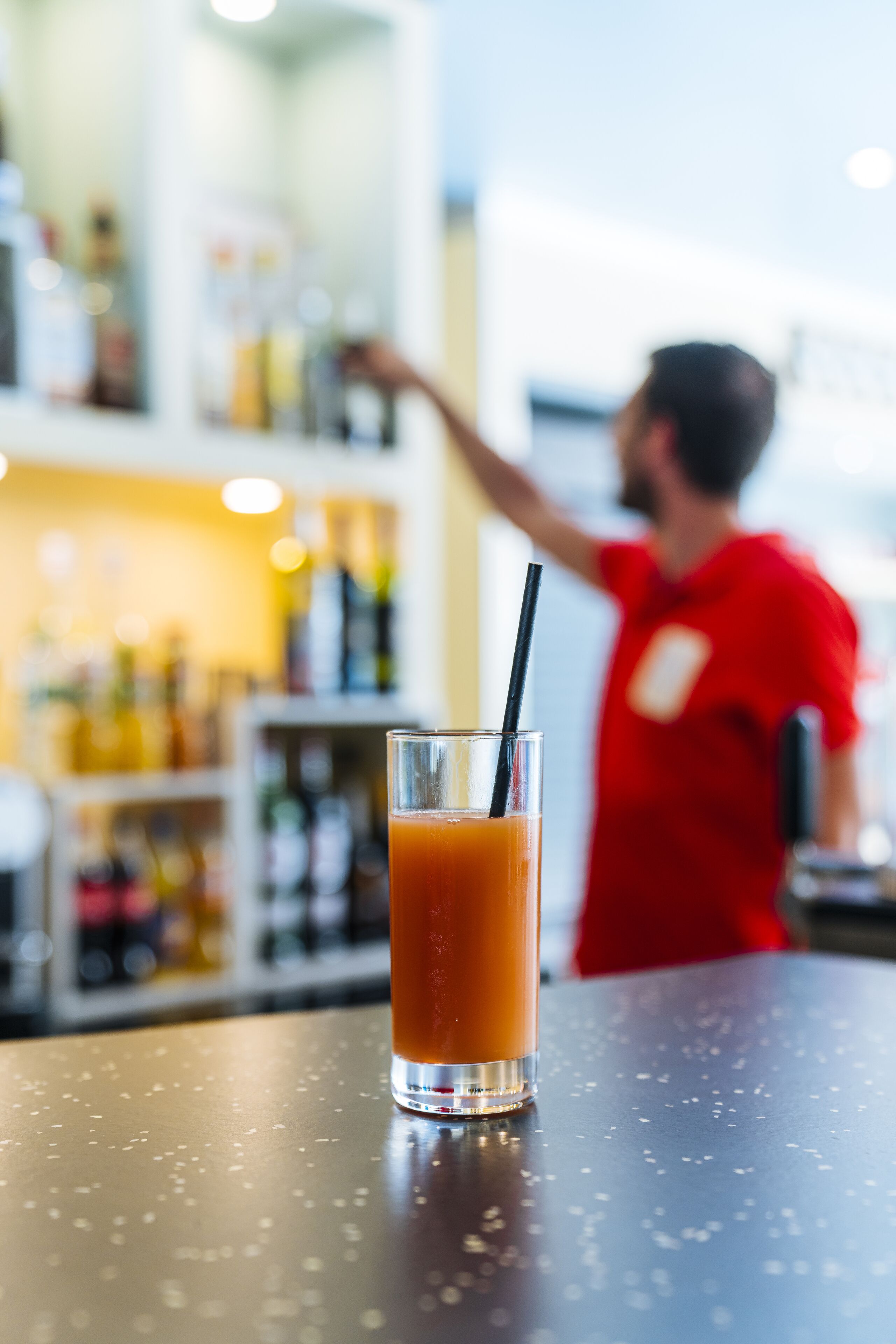 A bar setting with a glass of orange juice and a bartender in a red shirt.