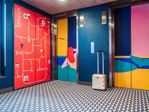 A hotel lobby with a colorful map, a suitcase, and a patterned floor. - ibis Styles Nice Aéroport Arenas (Nice)