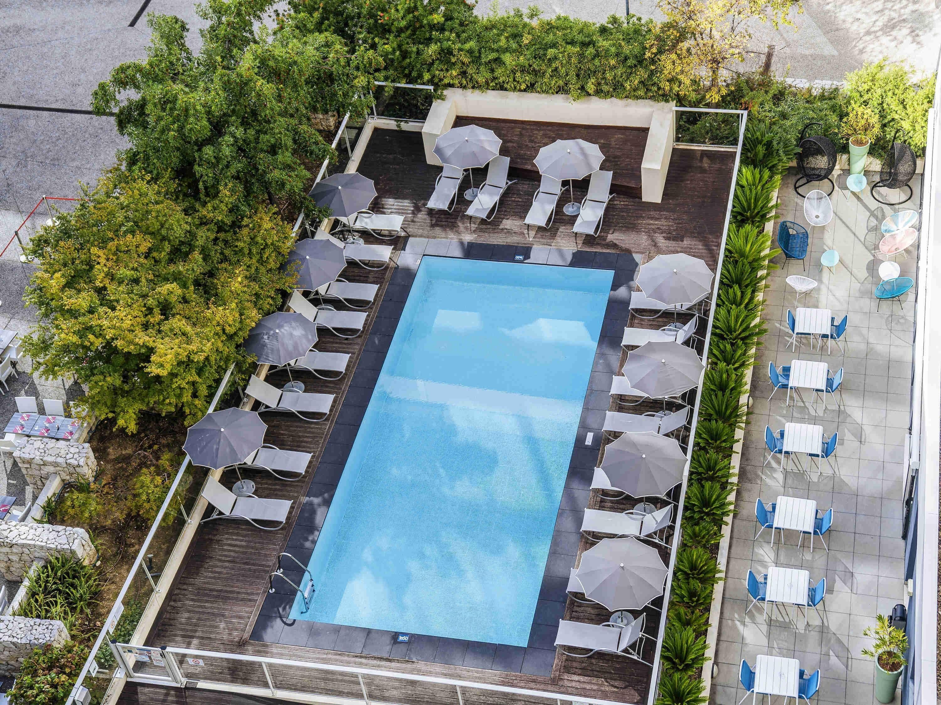 Vista a érea de un área de piscina en la azotea, con una piscina rectangular rodeada de sillones y sombrillas, y mobiliario exterior cercano con mesas y sillas.