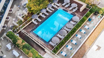 Vista aérea de una zona de piscina en la azotea con sillones de descanso y sombrillas, rodeada de vegetación y un área de comedor.