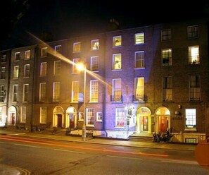 A multi-story building with illuminated windows and a street in front. - Glen Guesthouse (Dublin)