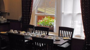 A dining area with a table set for four, chairs, a window with curtains, and a view of a garden. - Glen Guesthouse (Dublin)