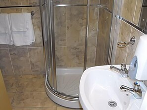 Un baño con cabina de ducha de vidrio, un lavamanos blanco y un perchero con toallas blancas.