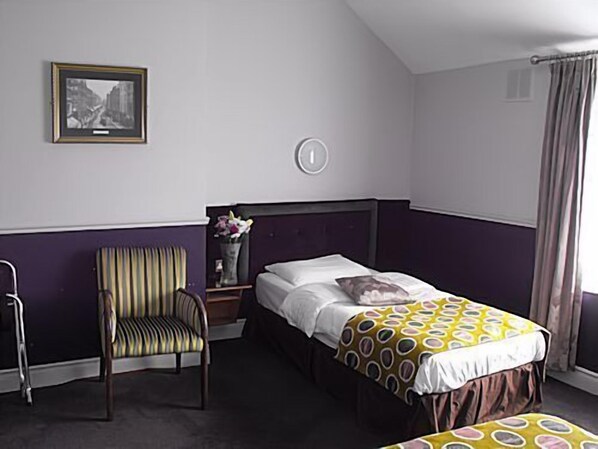 Un dormitorio con una cama, una silla, una mesita de noche y un cuadro en la pared.
