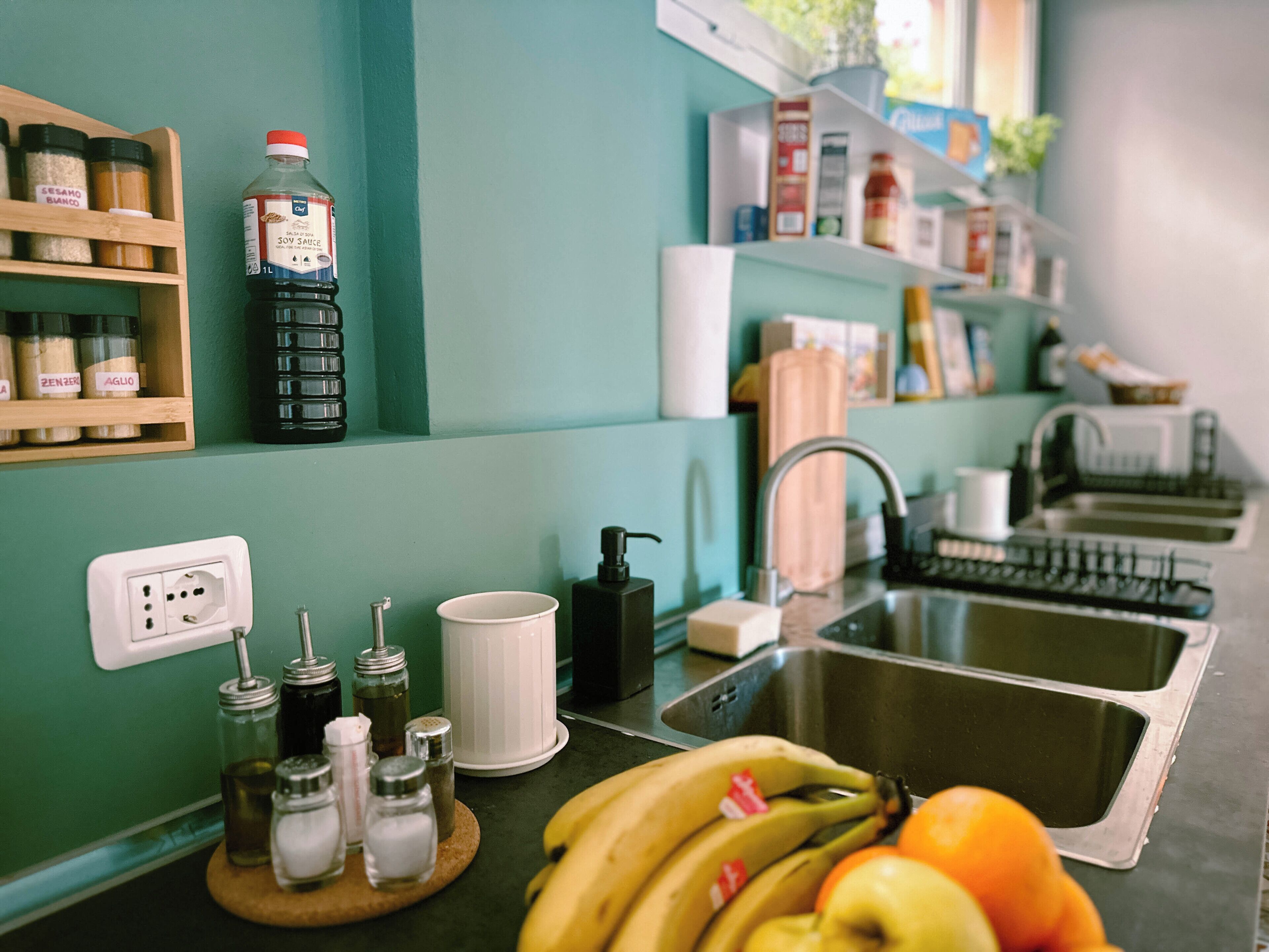 A kitchen with a sink, a countertop with jars, a bottle of soy sauce, and a banana on the counter.