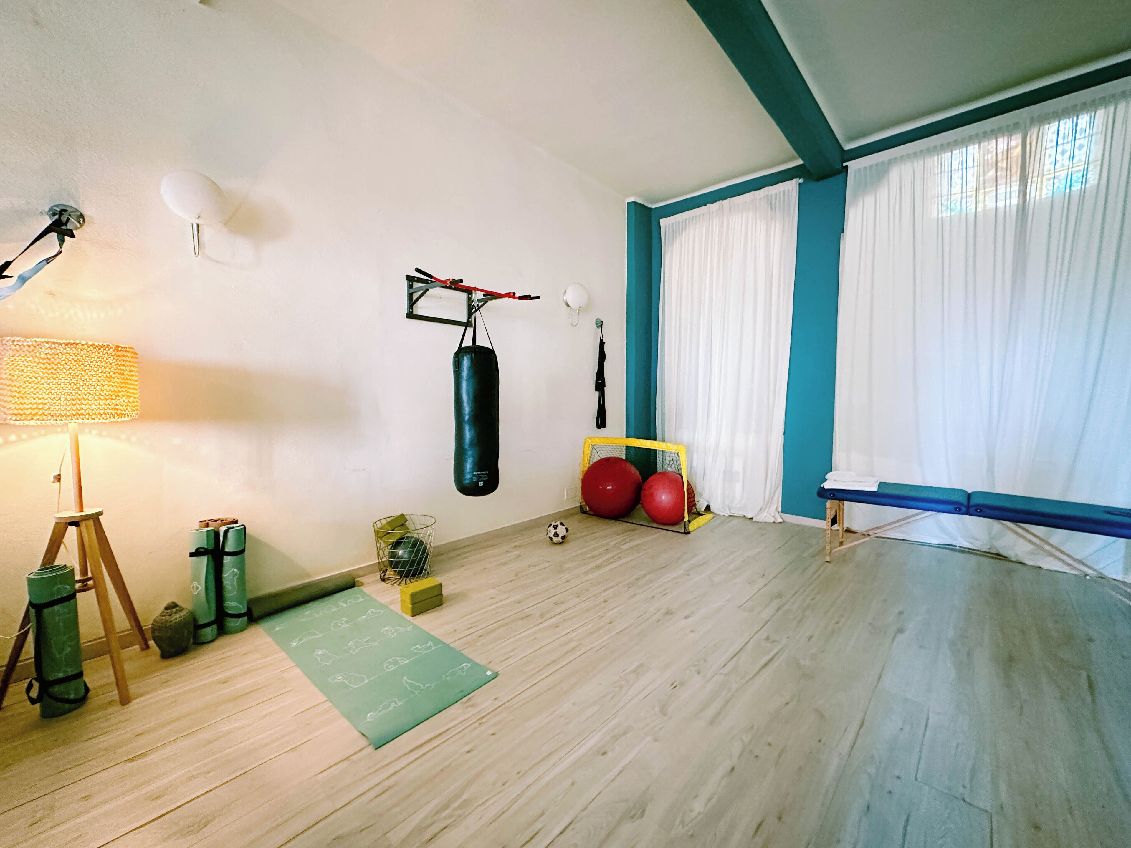 A room with a wooden floor, a punching bag, a soccer ball, and exercise equipment.