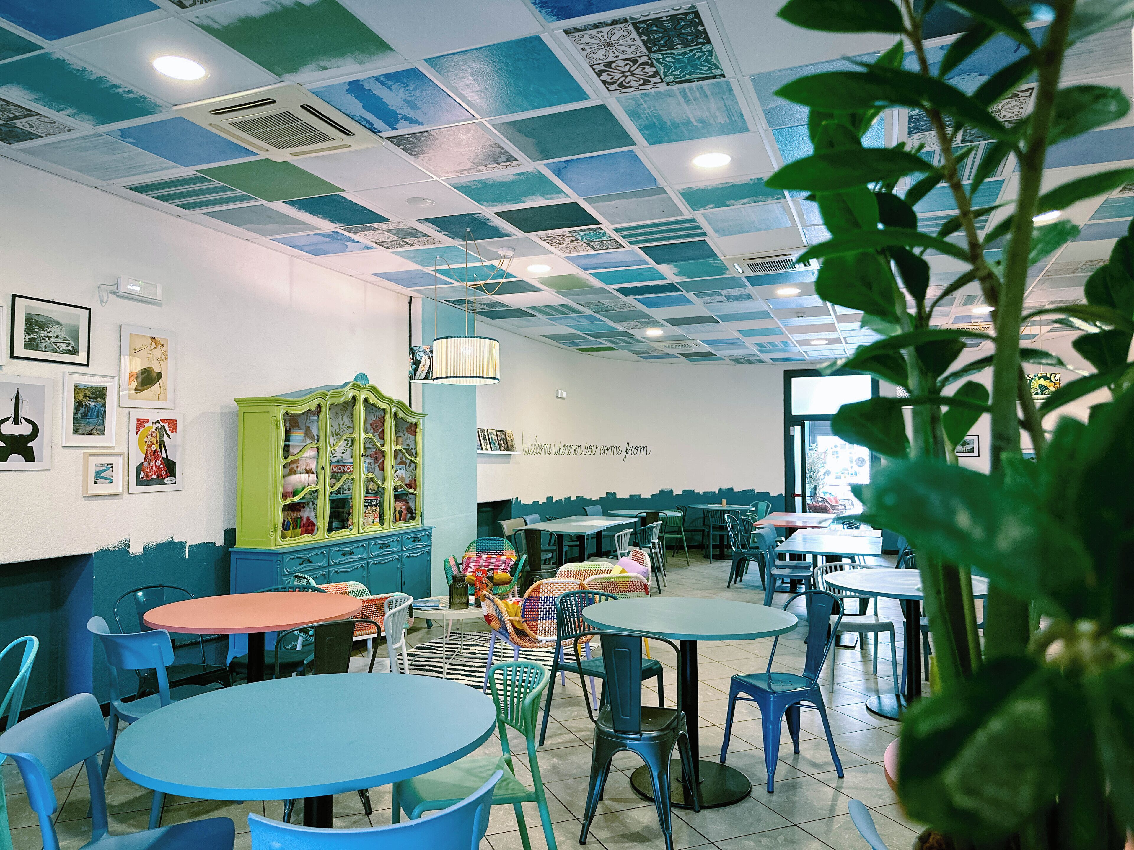 A cafe with multiple tables and chairs, a green cabinet, and a ceiling with a blue and white pattern.