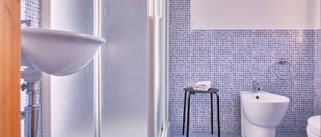 A bathroom with a white sink, a bidet, and a small stool.
