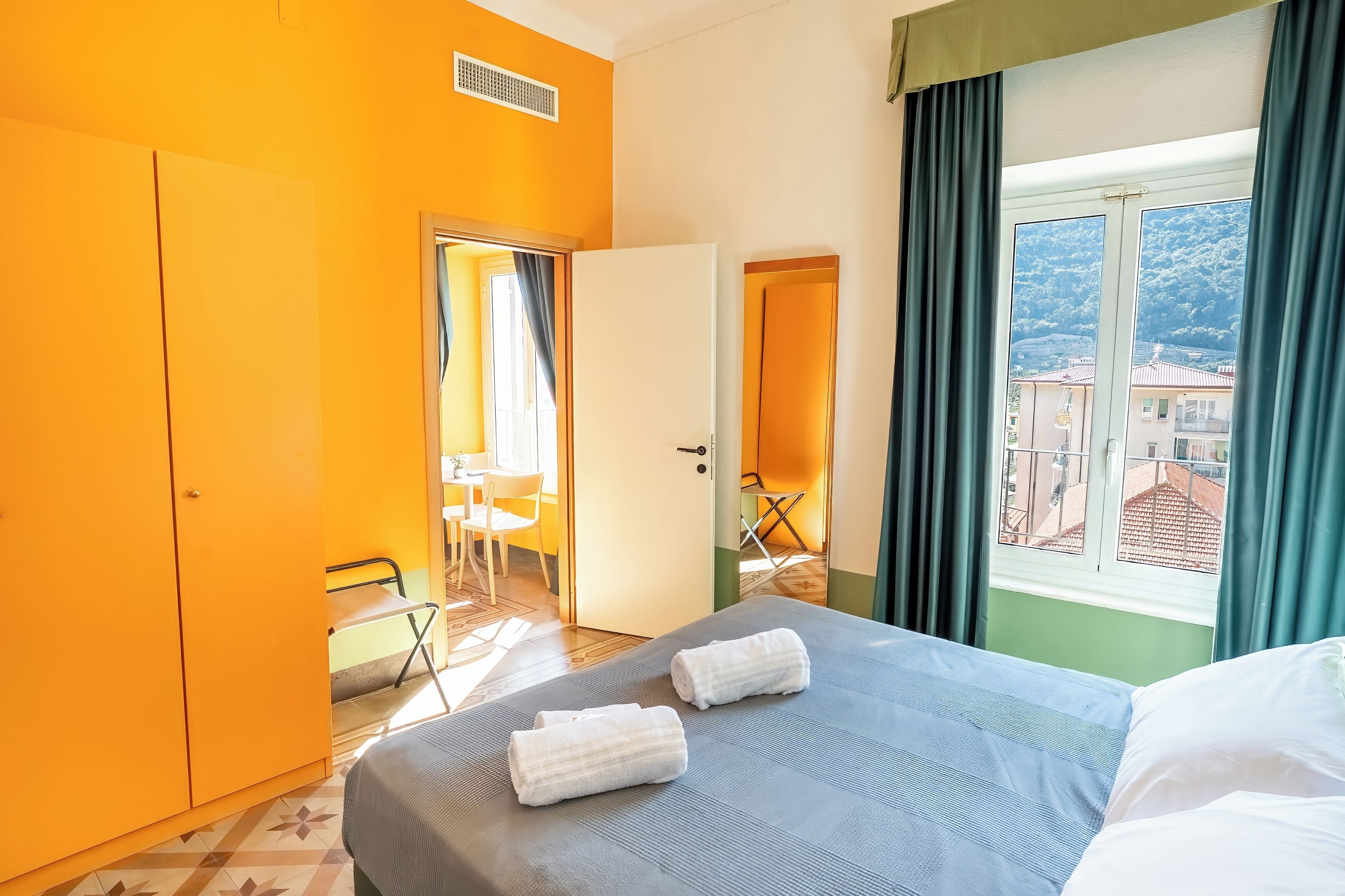A hotel room with a bed, a wardrobe, a window with a view, and a small table with chairs.
