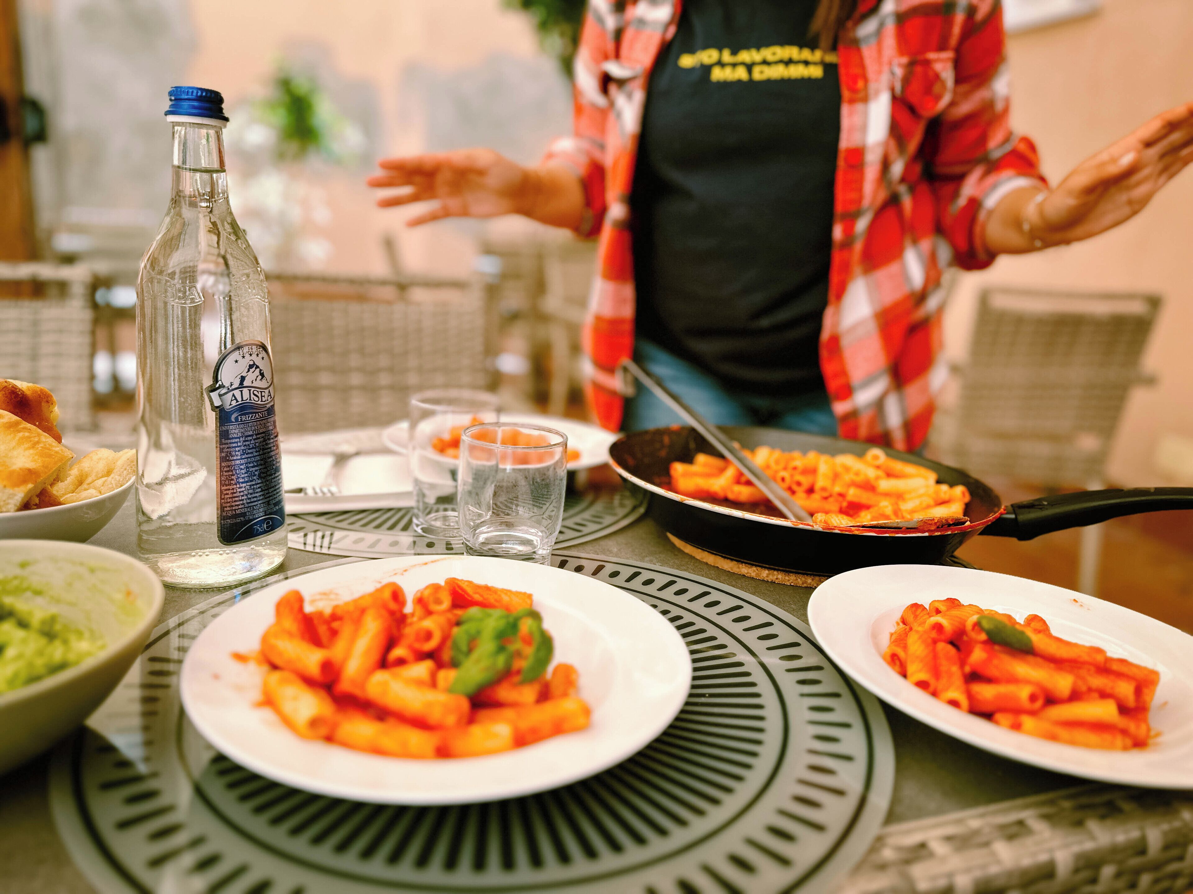 A dining table with plates of pasta, a bottle of Alisea sparkling water, and a pan with cooked pasta.