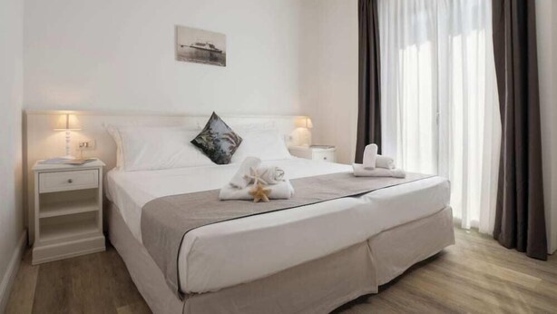 A hotel room with a large bed, bedside lamps, a nightstand, and a window with curtains. - Continental (Pietra Ligure)