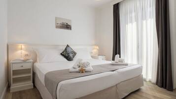 A neatly made bed with a pillow, a bedside lamp, a nightstand, and a window with curtains.