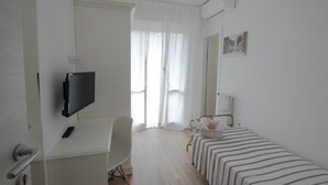 Une petite pièce propre, équipée d’un lit, d’un bureau, d’une chaise, d’un téléviseur et d’un radiateur.