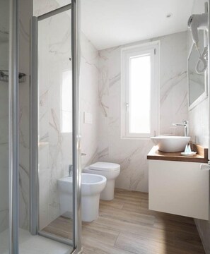 Un baño con cabina de ducha de vidrio, un lavabo con recipiente y un inodoro.