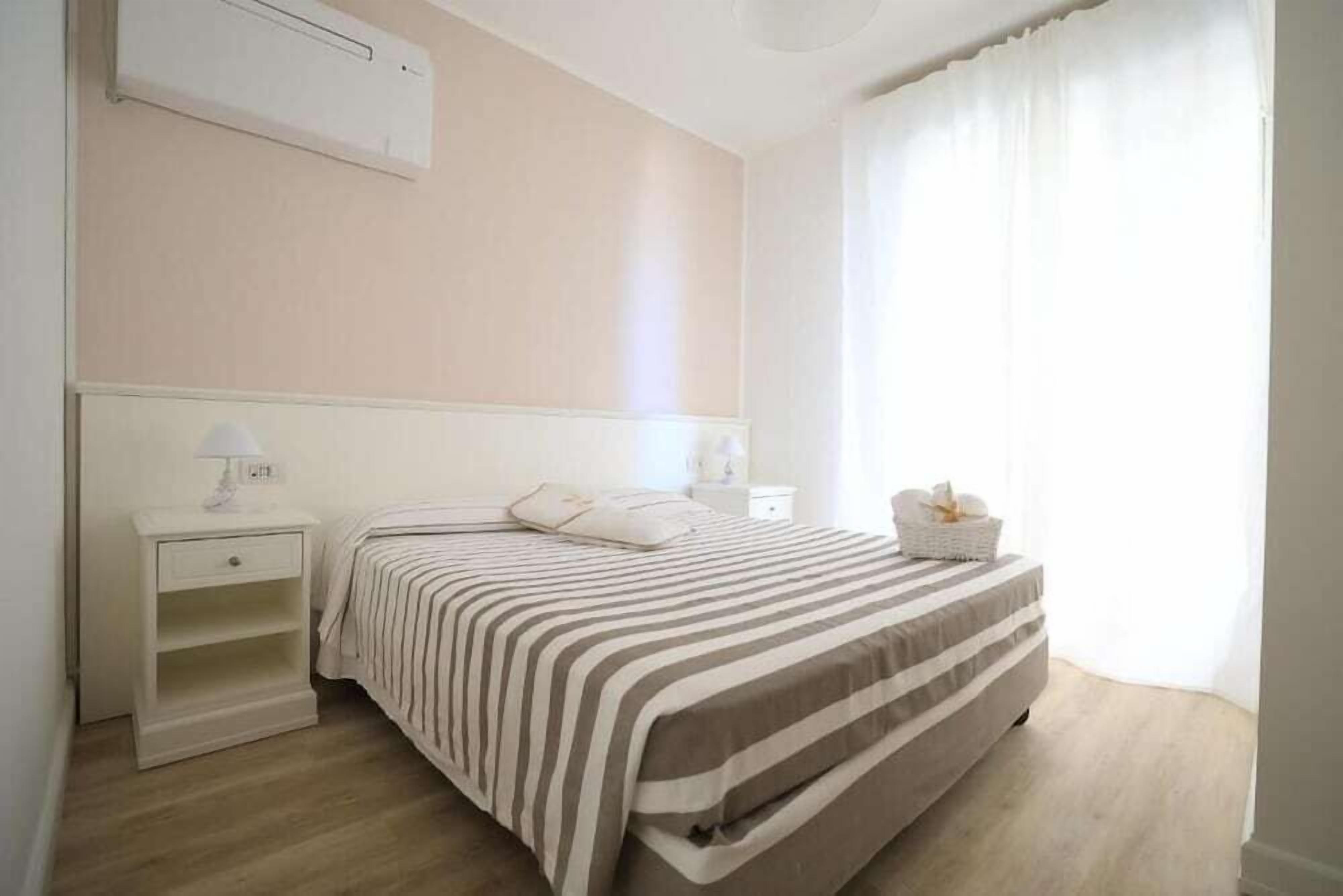 Een slaapkamer met een bed, nachtkastje, lamp en een raam met gordijnen.