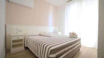 Een slaapkamer met een bed, nachtkastje, lamp en een raam met gordijnen.