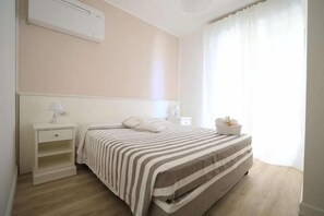 A bedroom with a bed, nightstand, lamp, and a window with curtains. - Continental (Pietra Ligure)
