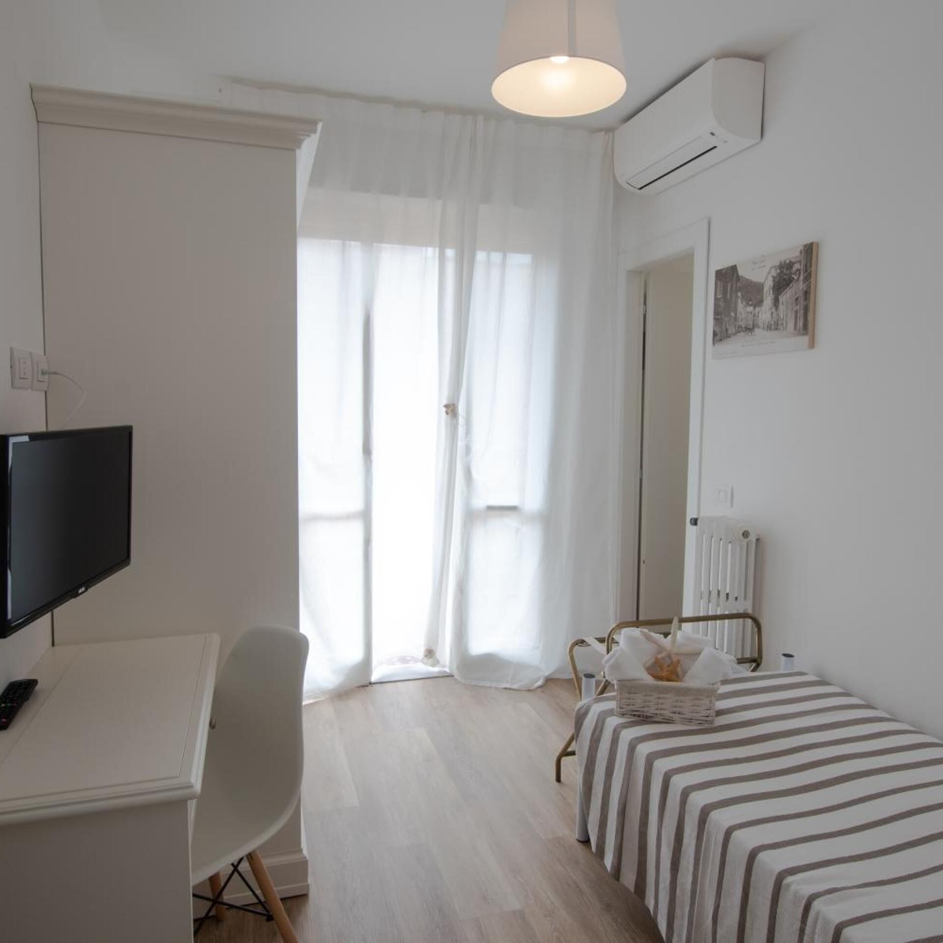Ein Hotelzimmer mit einem Bett, einem Schreibtisch mit Fernseher, einem Sessel, einem Heizkörper und einem Fenster mit Vorhängen.