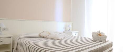 Une chambre à coucher comprenant un lit, des tables de chevet, une commode, une lampe, un panier et un appareil de climatisation.