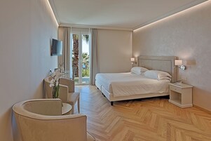Una habitación de hotel moderna con una cama grande, un escritorio con silla, un televisor montado en la pared y vistas a palmeras a través de la ventana.
