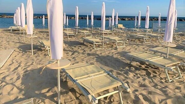 A beach with rows of white sun loungers and umbrellas, a clear sky, and calm sea in the background. - Hotel Paradiso (Sanremo)