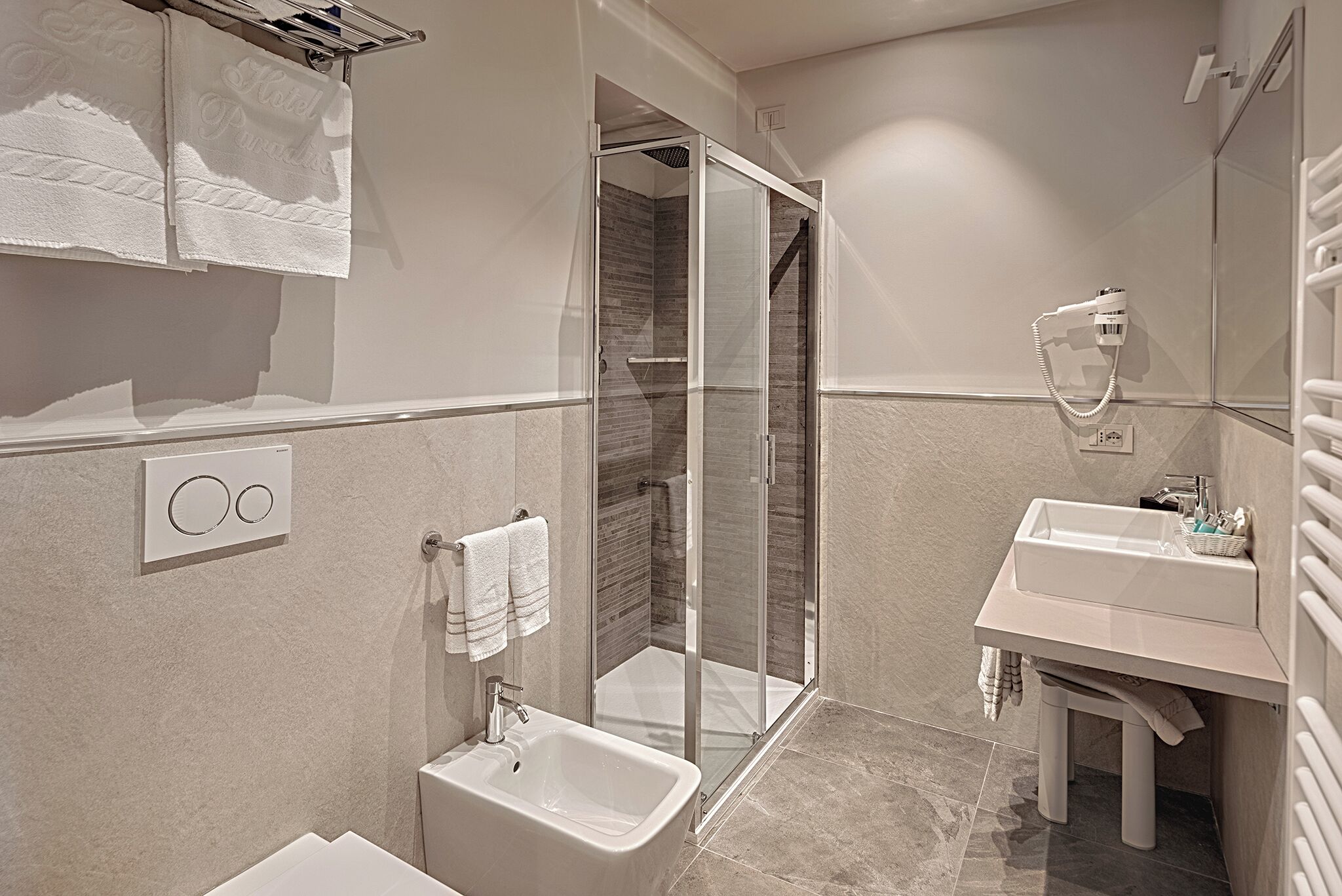 A modern bathroom with a glass-enclosed shower, a standalone sink, and a towel rack with a hotel towel.