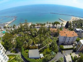 Vista aérea de uma área costeira com praia, um cais e um complexo residencial com um pátio central rodeado por vegetação.