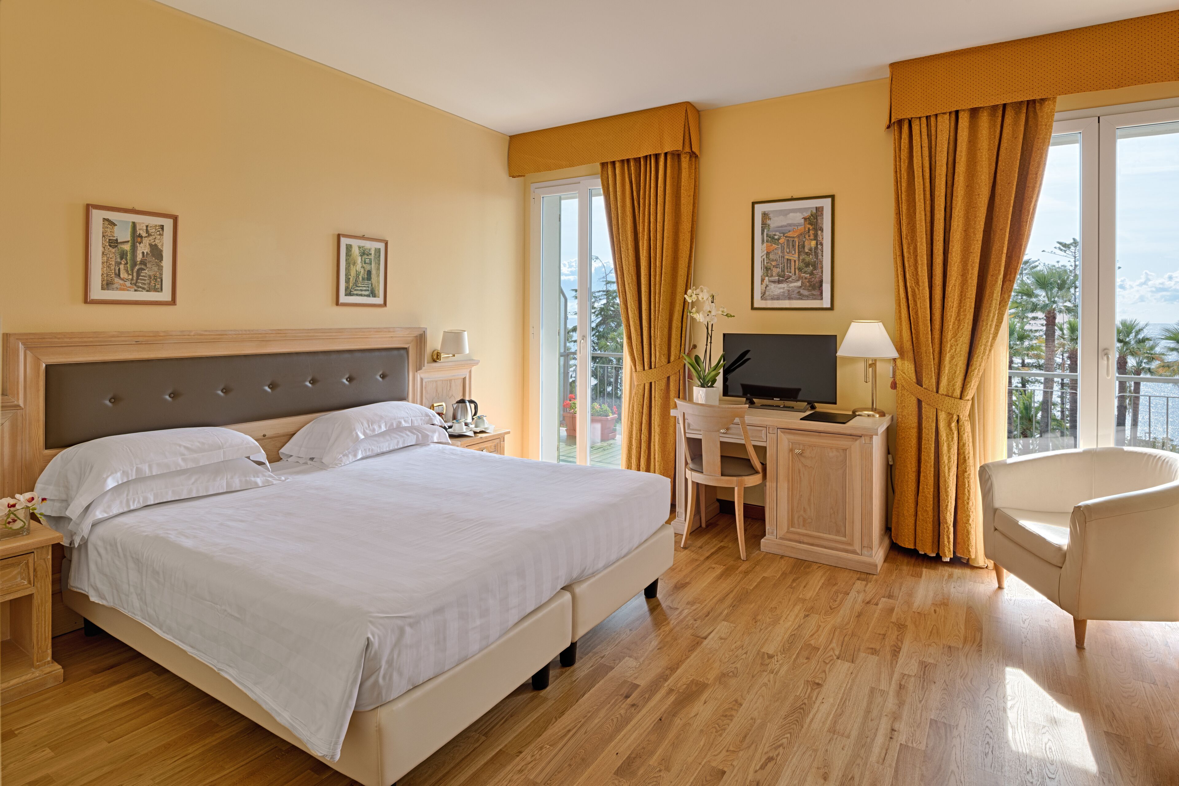 Habitación de hotel con una cama grande, un escritorio con computadora, una silla y un balcón con cortinas.
