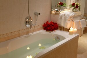 Una bañera con velas, un cabezal de ducha y un ramo de flores rojas.