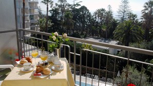 A balcony with a table set for breakfast, including croissants, juice, and a vase of flowers. - Hotel Paradiso (Sanremo)