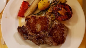 Un plato con bistec a la parrilla, verduras asadas y tomate a la plancha.