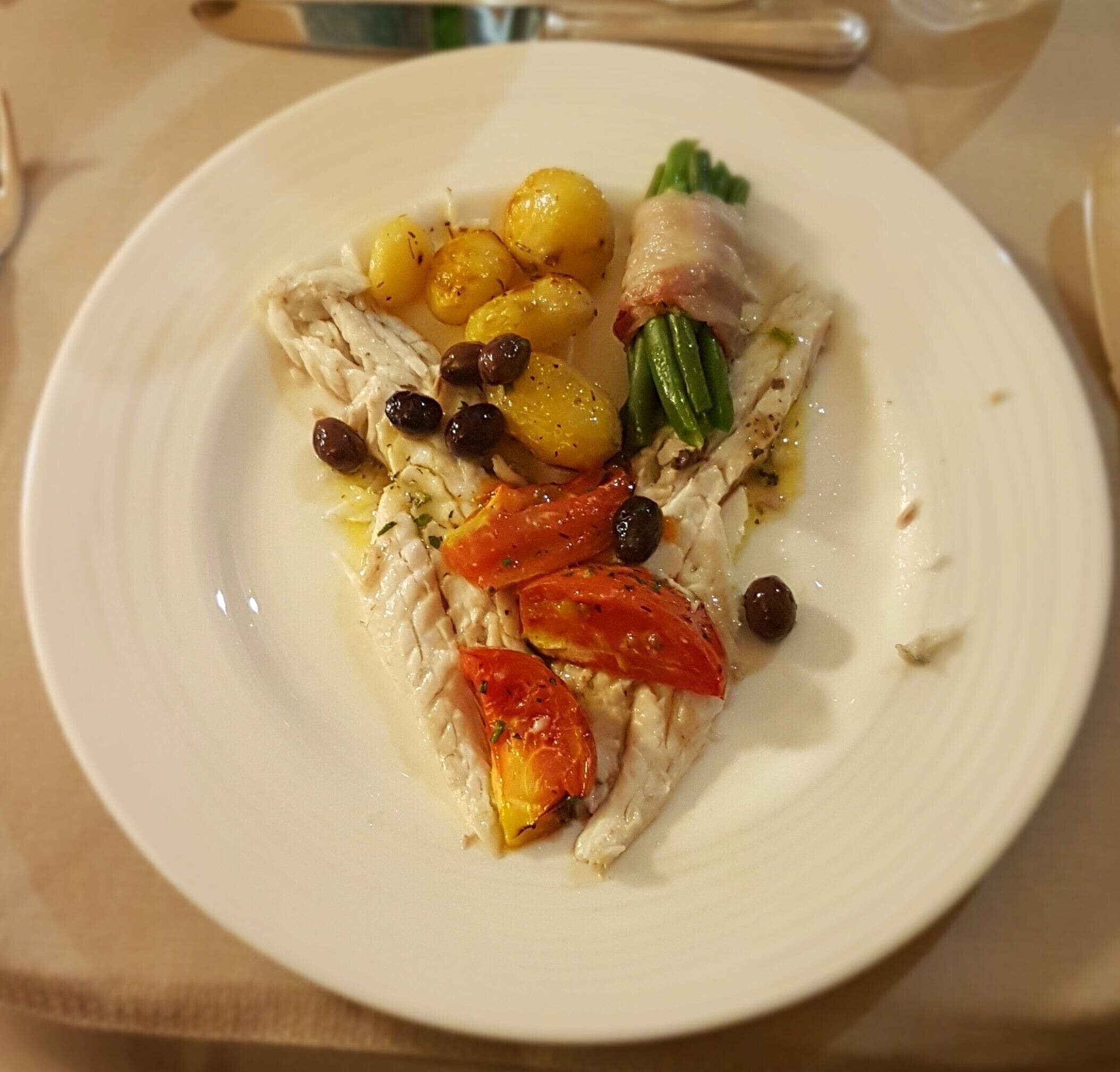 A plate with grilled chicken, roasted potatoes, cherry tomatoes, and olives.
