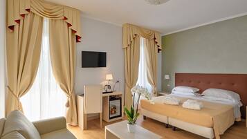 Ein Hotelzimmer mit Bett, Sofa, kleinem Tisch mit Pflanze, Fernseher und Minibar.
