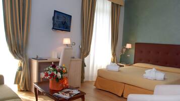 Una habitación de hotel con cama, escritorio, silla, una mesa con un jarrón de flores y televisor en la pared.