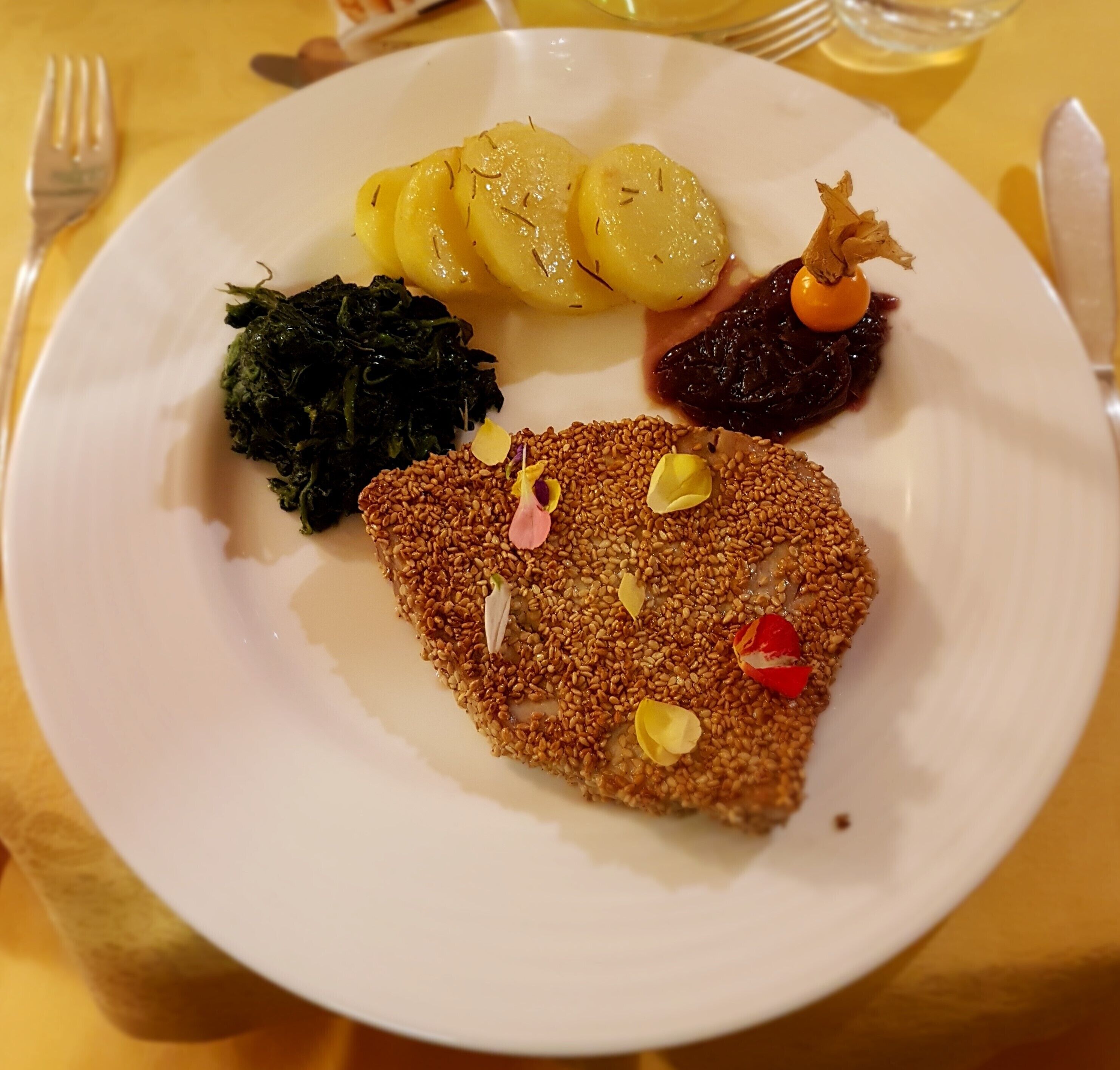 A plate with a breaded cutlet, boiled potatoes, greens, and a fruit garnish.