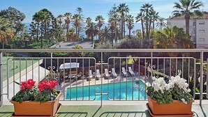A balcony with a pool, palm trees, and lounge chairs. - Hotel Paradiso (Sanremo)