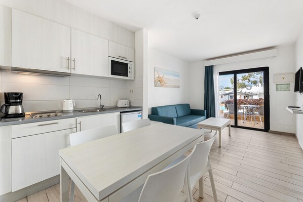 A modern kitchen with white cabinets, a microwave, and a coffee maker. There is a dining area with a table and chairs, and a blue sofa.