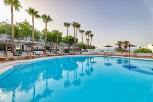 Piscina con sillones de descanso y palmeras.
