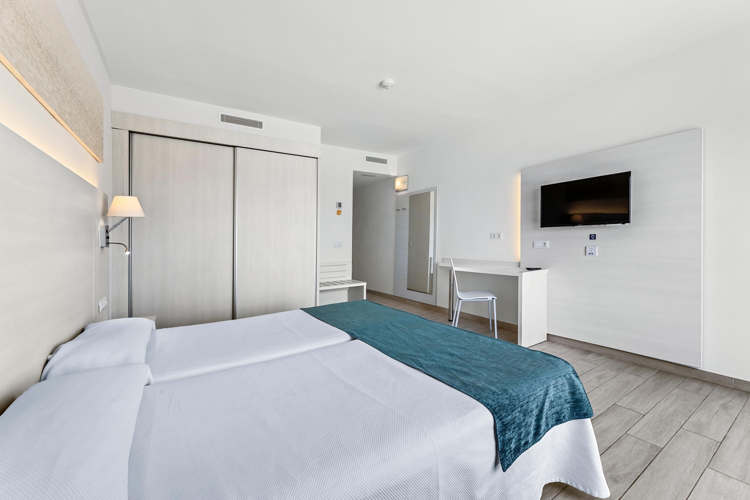 A modern hotel room with a bed, a desk, a chair, a TV, and a wardrobe.