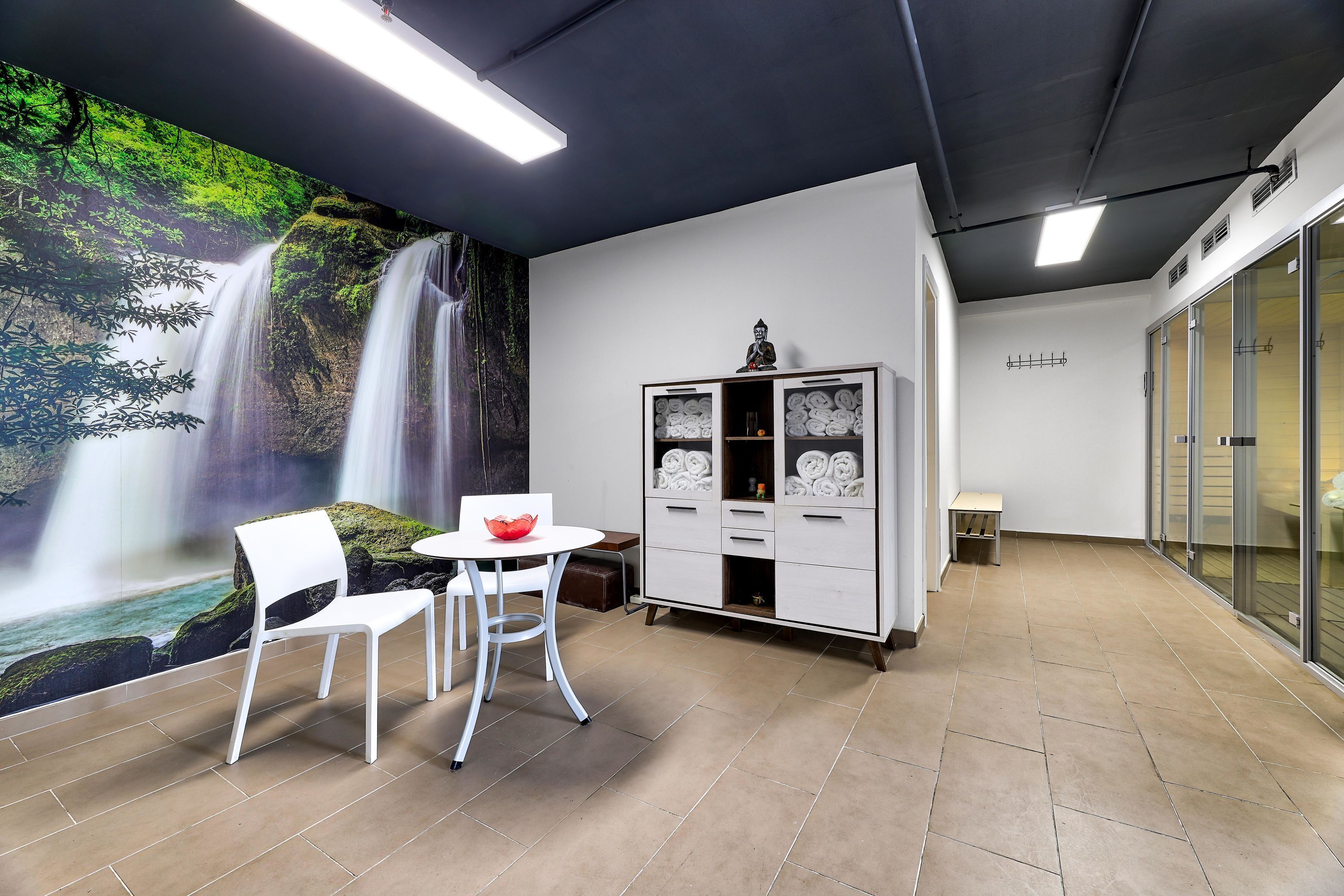 Una habitación con un mural de cascada, un armario blanco con objetos decorativos, y una pequeña mesa con sillas.