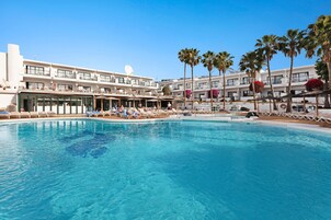 Un hotel con piscina, tumbonas y palmeras.