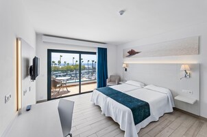Habitación de hotel moderna con una cama grande, un escritorio y vistas a palmeras y al paisaje urbano a través de una puerta corrediza.