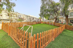A fenced courtyard with artificial grass, trees, and a building with balconies. - THB Flora Aparthotel (Tías)