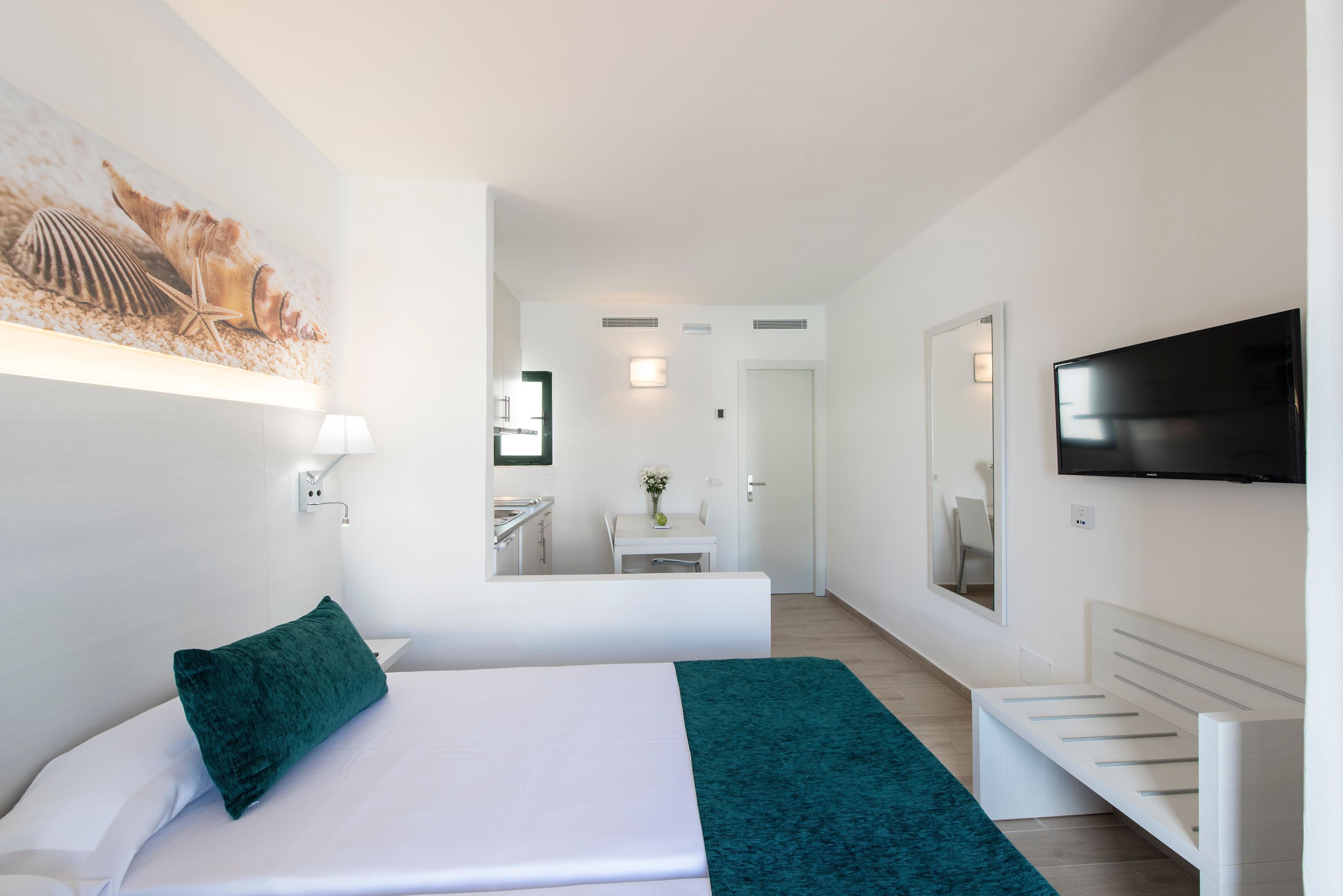 Une chambre d’hôtel avec un lit, un bureau, une chaise, une télévision et une salle de bain visible à travers une porte ouverte.
