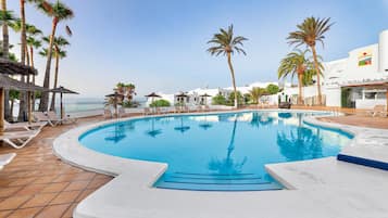 Zona de piscina con vista despejada al océano, rodeada de palmeras y sillas de descanso.