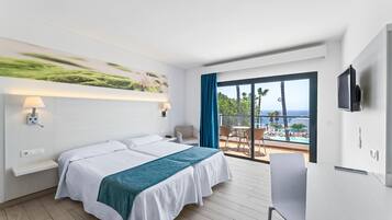 Een hotelkamer met een bed, een bureau, een televisie en een balkon met uitzicht op zee.