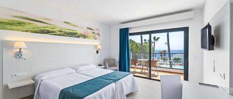 A hotel room with a bed, a desk, a TV, and a balcony with a view of the sea.