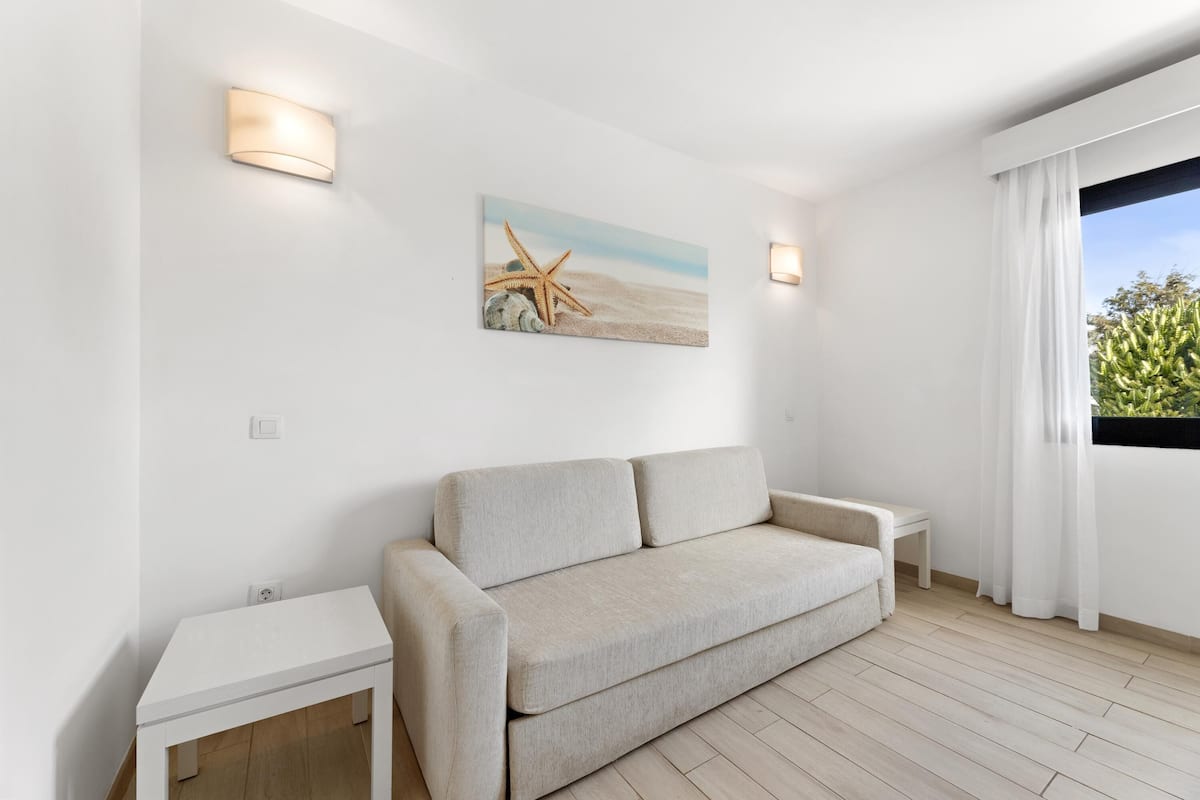A minimalist room with a beige sofa, a small white table, and a painting of a beach scene.